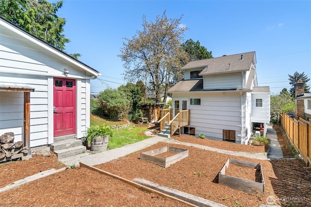 rear view of house featuring fence, a shingled roof, entry steps, and a vegetable garden