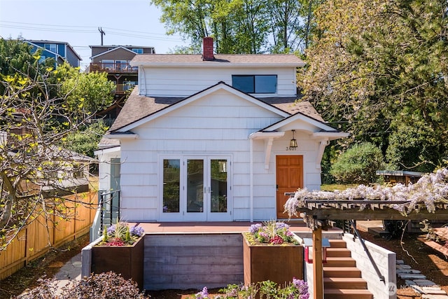 bungalow-style house featuring fence, french doors, a chimney, stairs, and a shingled roof