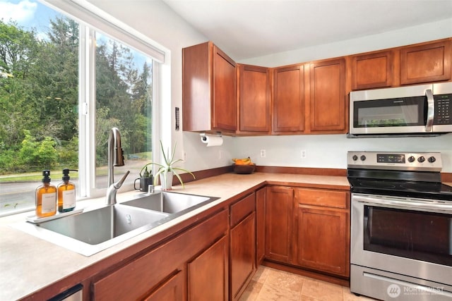 kitchen with a sink, light countertops, stainless steel appliances, and brown cabinets
