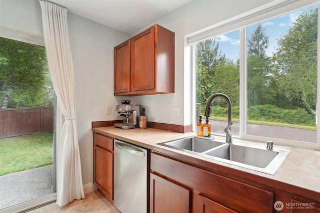 kitchen with stainless steel dishwasher, a sink, brown cabinets, and light countertops