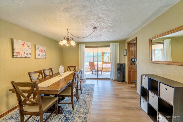 dining room featuring a textured ceiling, light wood finished floors, a notable chandelier, and a textured wall
