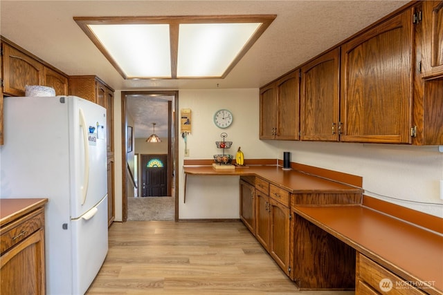 kitchen featuring light wood-style floors, freestanding refrigerator, and brown cabinets