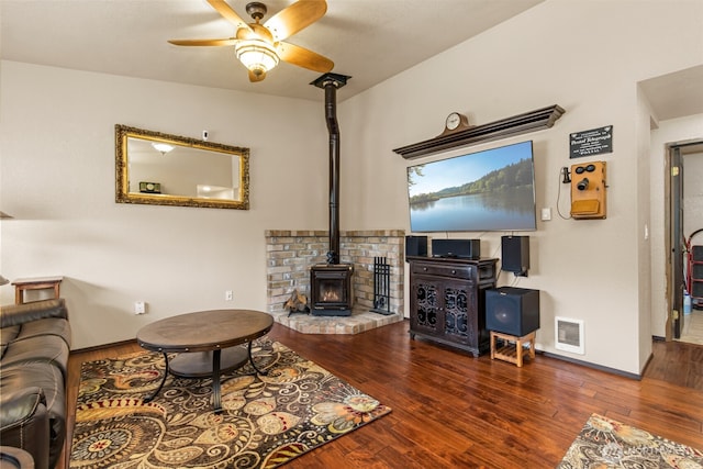 living area with a wood stove, a ceiling fan, baseboards, wood finished floors, and visible vents