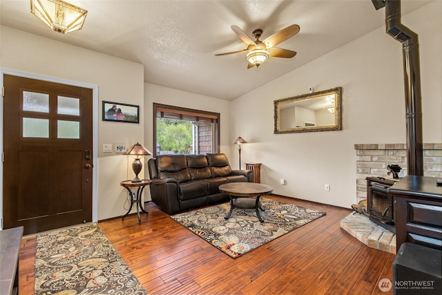 living room featuring ceiling fan, a wood stove, wood finished floors, and lofted ceiling