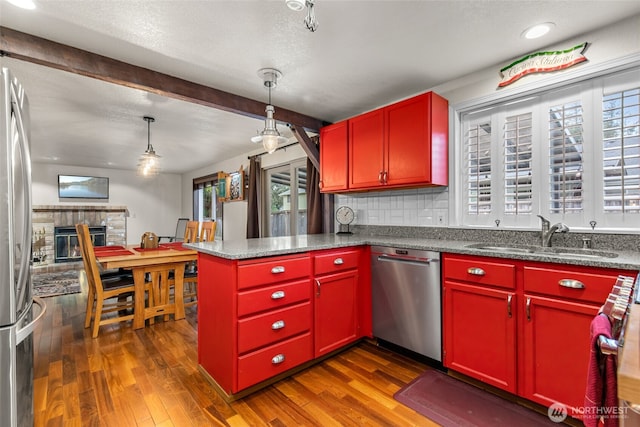 kitchen with a peninsula, a glass covered fireplace, red cabinets, a sink, and appliances with stainless steel finishes