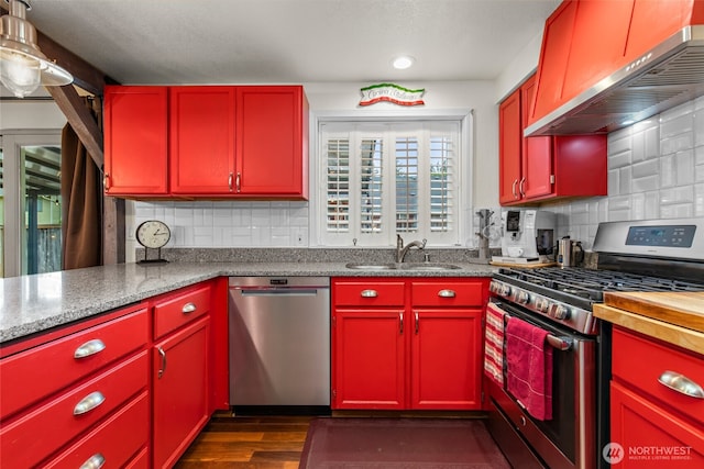 kitchen featuring a sink, appliances with stainless steel finishes, red cabinets, and wall chimney exhaust hood