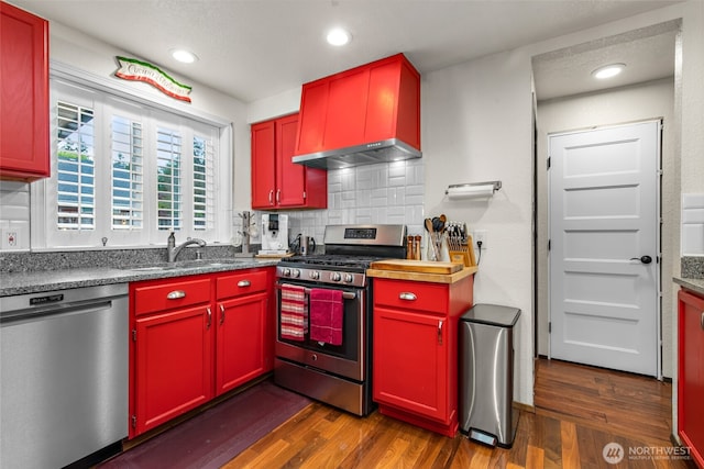 kitchen with red cabinetry, dark wood-style flooring, tasteful backsplash, a sink, and stainless steel appliances