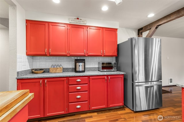 kitchen featuring red cabinetry, freestanding refrigerator, wood finished floors, tasteful backsplash, and visible vents
