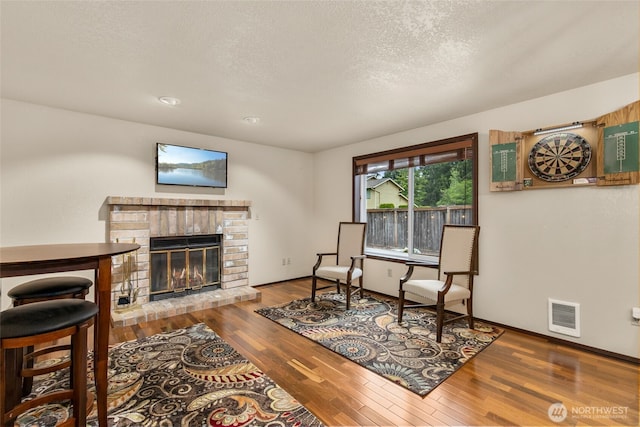 sitting room with visible vents, wood finished floors, a fireplace, baseboards, and a textured ceiling