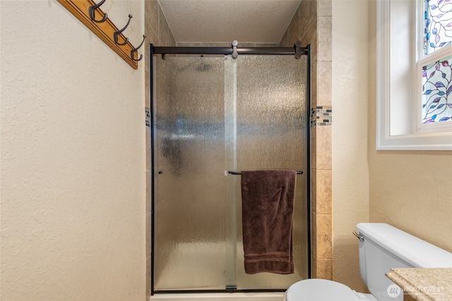 bathroom with a textured wall, a shower stall, and toilet