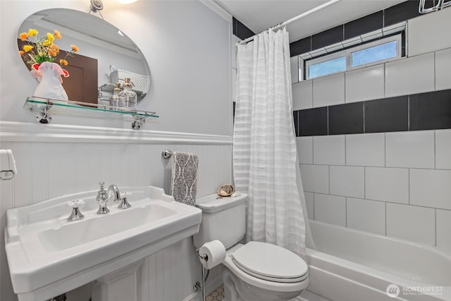 bathroom featuring a sink, wainscoting, shower / tub combo with curtain, and toilet
