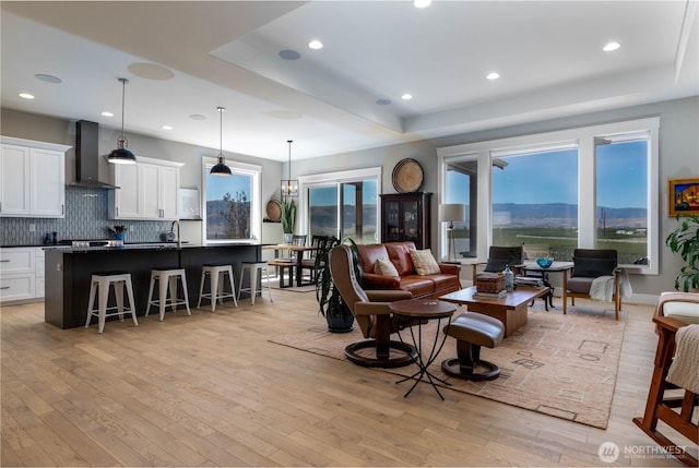 living room featuring light wood-type flooring, recessed lighting, and a raised ceiling