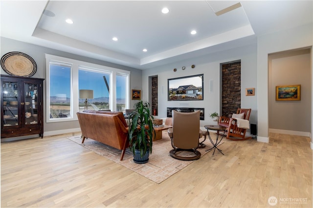 living area with baseboards, recessed lighting, a tray ceiling, and light wood-style flooring