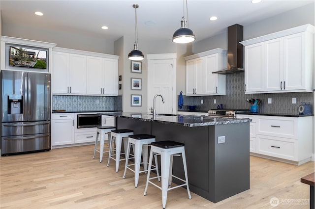 kitchen featuring a kitchen breakfast bar, wall chimney exhaust hood, tasteful backsplash, a sink, and appliances with stainless steel finishes