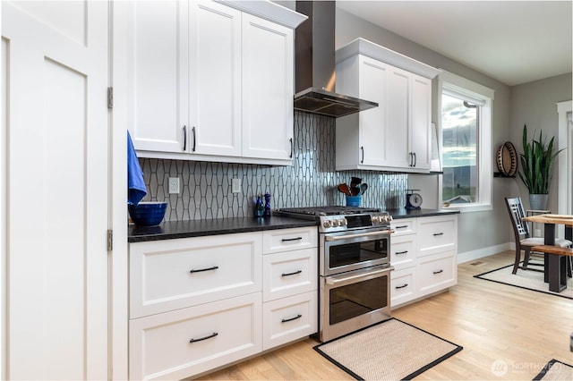 kitchen with light wood-type flooring, wall chimney exhaust hood, backsplash, and range with two ovens