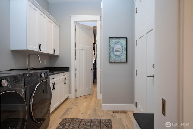 laundry room with cabinet space, a sink, baseboards, light wood-style floors, and washer and clothes dryer