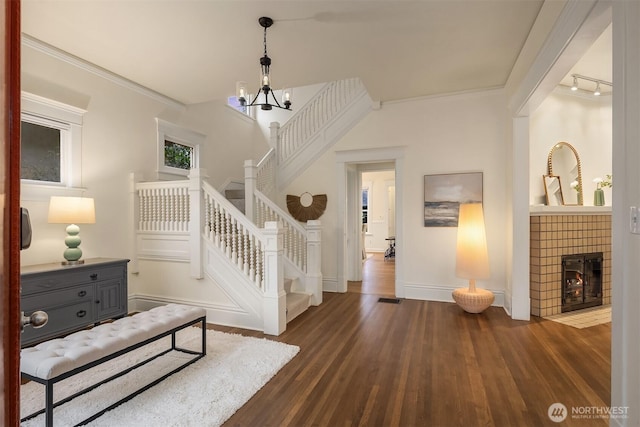 bedroom with dark wood-style floors, baseboards, crown molding, a tiled fireplace, and a chandelier