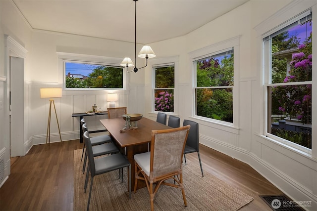 dining area featuring a decorative wall, dark wood finished floors, and wainscoting