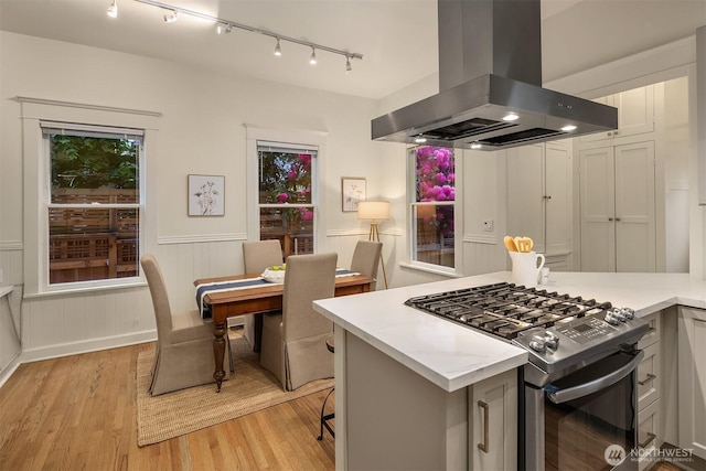 kitchen featuring island range hood, stainless steel range with gas cooktop, track lighting, light wood-type flooring, and light countertops