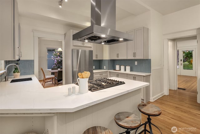 kitchen featuring island exhaust hood, a sink, freestanding refrigerator, gas cooktop, and a kitchen breakfast bar