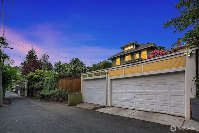 garage at dusk featuring fence