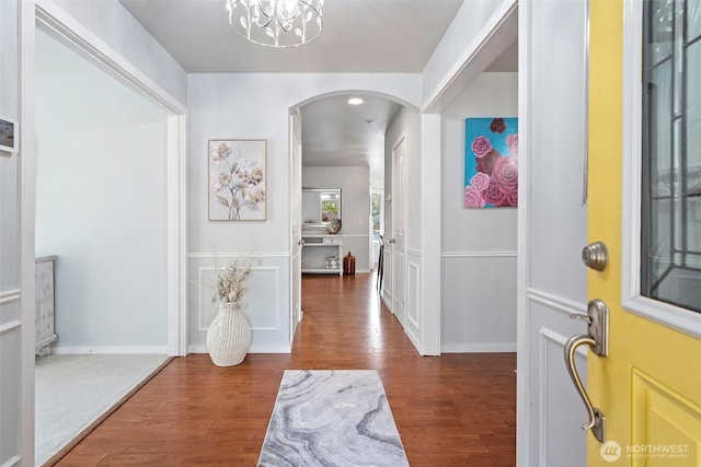 entryway featuring an inviting chandelier, arched walkways, baseboards, and wood finished floors