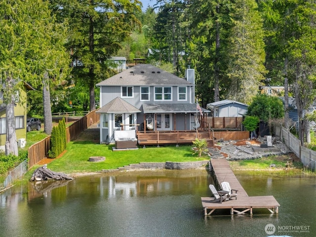 back of property with a shingled roof, a deck with water view, a fenced backyard, a chimney, and a yard