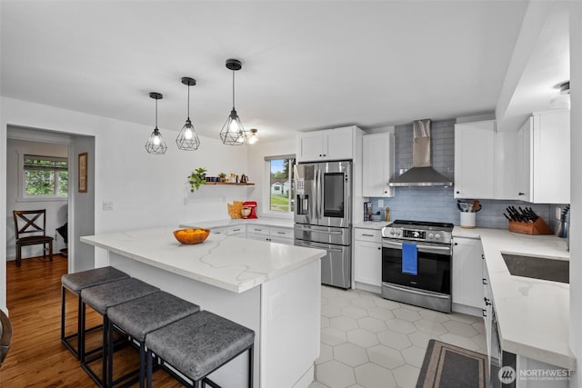 kitchen with a breakfast bar area, wall chimney range hood, tasteful backsplash, light stone counters, and stainless steel appliances