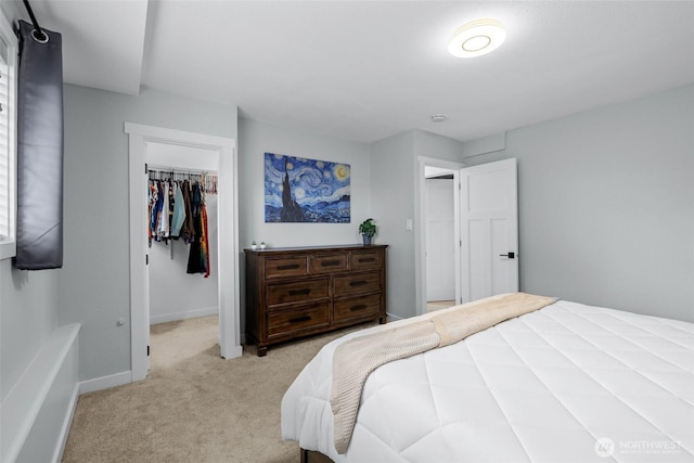 bedroom featuring baseboards, light colored carpet, a walk in closet, and a closet