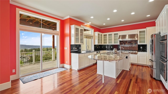 kitchen with exhaust hood, crown molding, and a kitchen island with sink