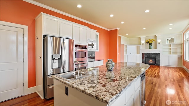 kitchen with crown molding, white cabinets, light wood-style floors, stainless steel appliances, and a center island with sink