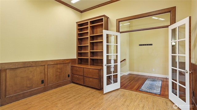 interior space featuring a wainscoted wall, ornamental molding, french doors, and light wood-type flooring
