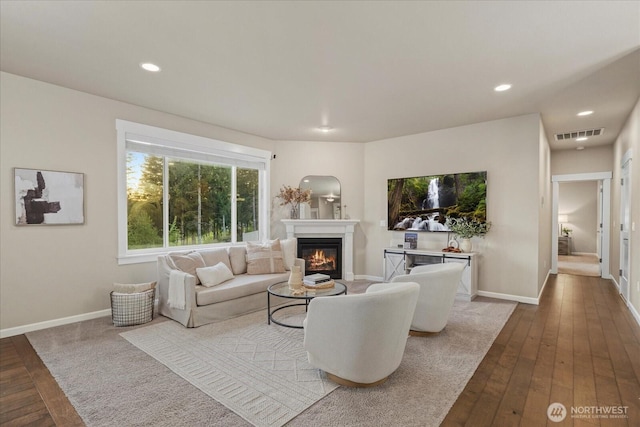 living room with wood-type flooring, a glass covered fireplace, recessed lighting, baseboards, and visible vents