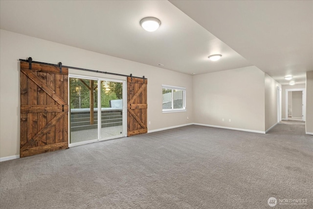unfurnished living room featuring baseboards, a barn door, and carpet