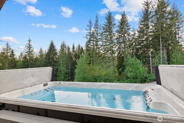 view of swimming pool featuring a covered hot tub and a forest view