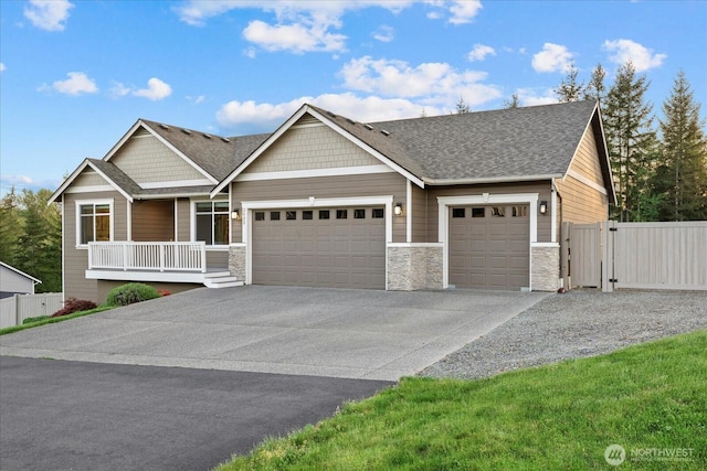 view of front facade featuring fence, stone siding, an attached garage, driveway, and a porch