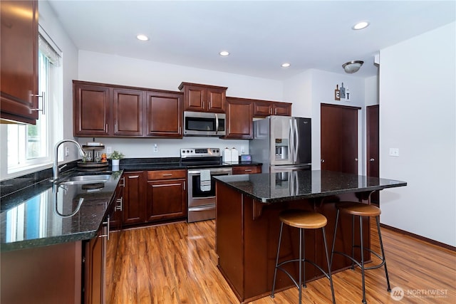 kitchen with a center island, a sink, light wood-style floors, a breakfast bar, and stainless steel appliances