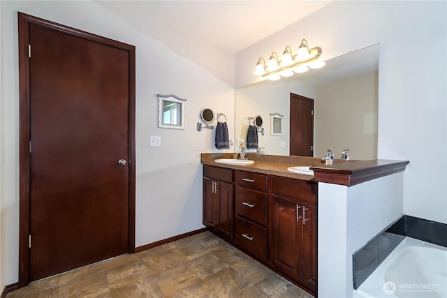 bathroom with a sink, double vanity, stone finish floor, baseboards, and a bath