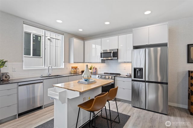 kitchen featuring light wood-style floors, a kitchen bar, a sink, appliances with stainless steel finishes, and backsplash