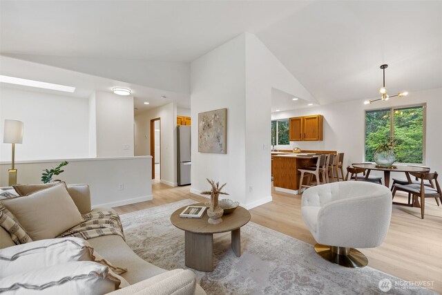 living area with light wood-style flooring, a notable chandelier, vaulted ceiling, and a wealth of natural light