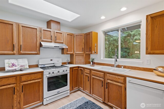 kitchen featuring a sink, light countertops, under cabinet range hood, and white appliances
