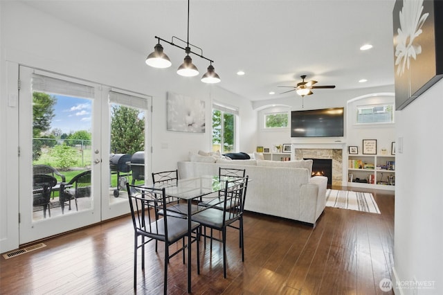 dining room featuring visible vents, a stone fireplace, dark wood-type flooring, french doors, and a ceiling fan