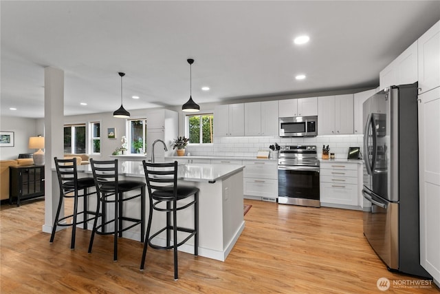 kitchen with a kitchen island with sink, backsplash, appliances with stainless steel finishes, light countertops, and white cabinets