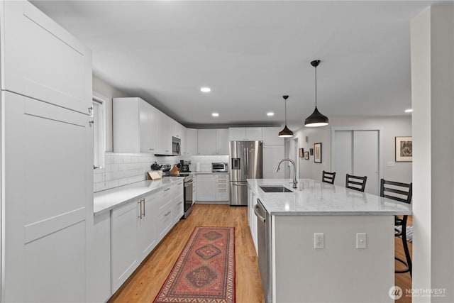 kitchen with decorative backsplash, light wood-style floors, white cabinetry, a sink, and stainless steel appliances