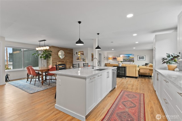kitchen featuring open floor plan, a sink, light wood finished floors, and white cabinetry
