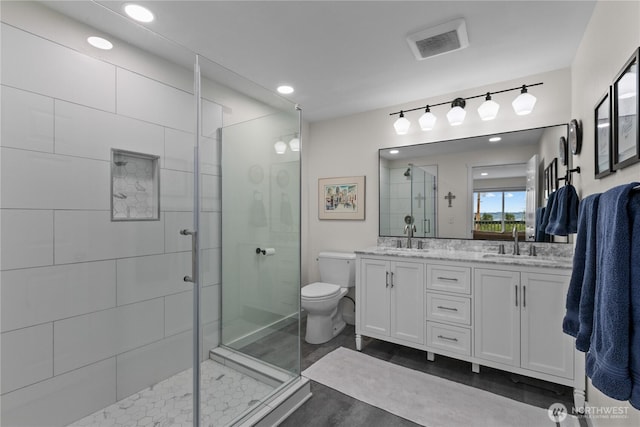 bathroom featuring visible vents, double vanity, toilet, a shower stall, and a sink