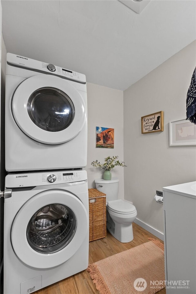 washroom with baseboards, laundry area, stacked washer / dryer, and wood finished floors