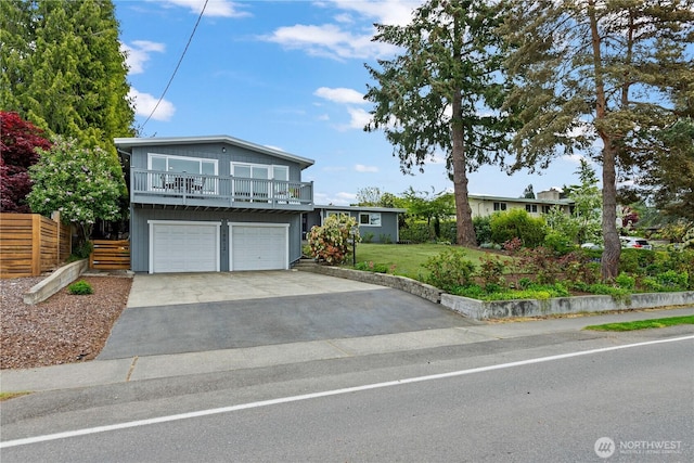 tri-level home with fence, an attached garage, a front yard, a balcony, and driveway
