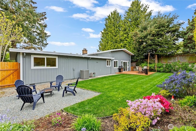 rear view of property with a lawn, a patio area, central AC, fence, and an outdoor fire pit
