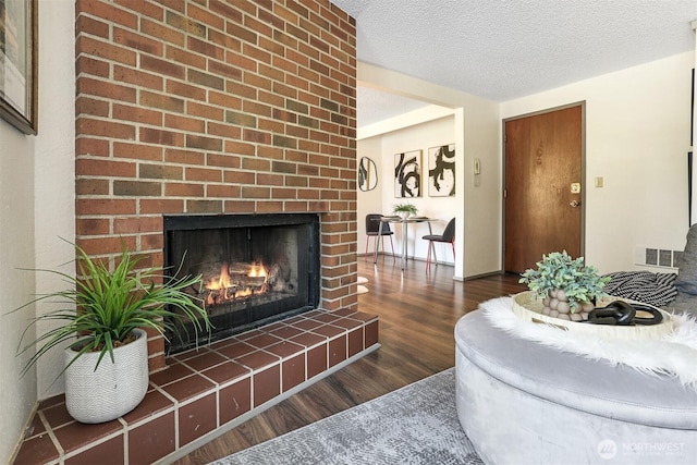living room featuring visible vents, a textured ceiling, wood finished floors, and a fireplace